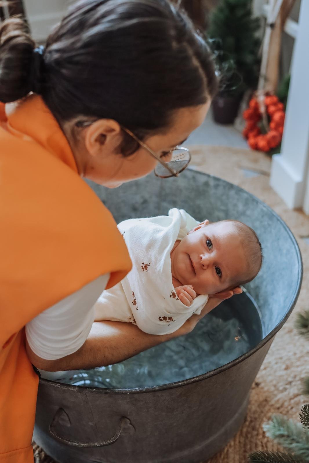 Une femme regarde tendrement un bébé dans un bain ou une cuve, tenant la tête du bébé avec ses mains. Le bébé a l'air heureux, regardant vers l'appareil photo.