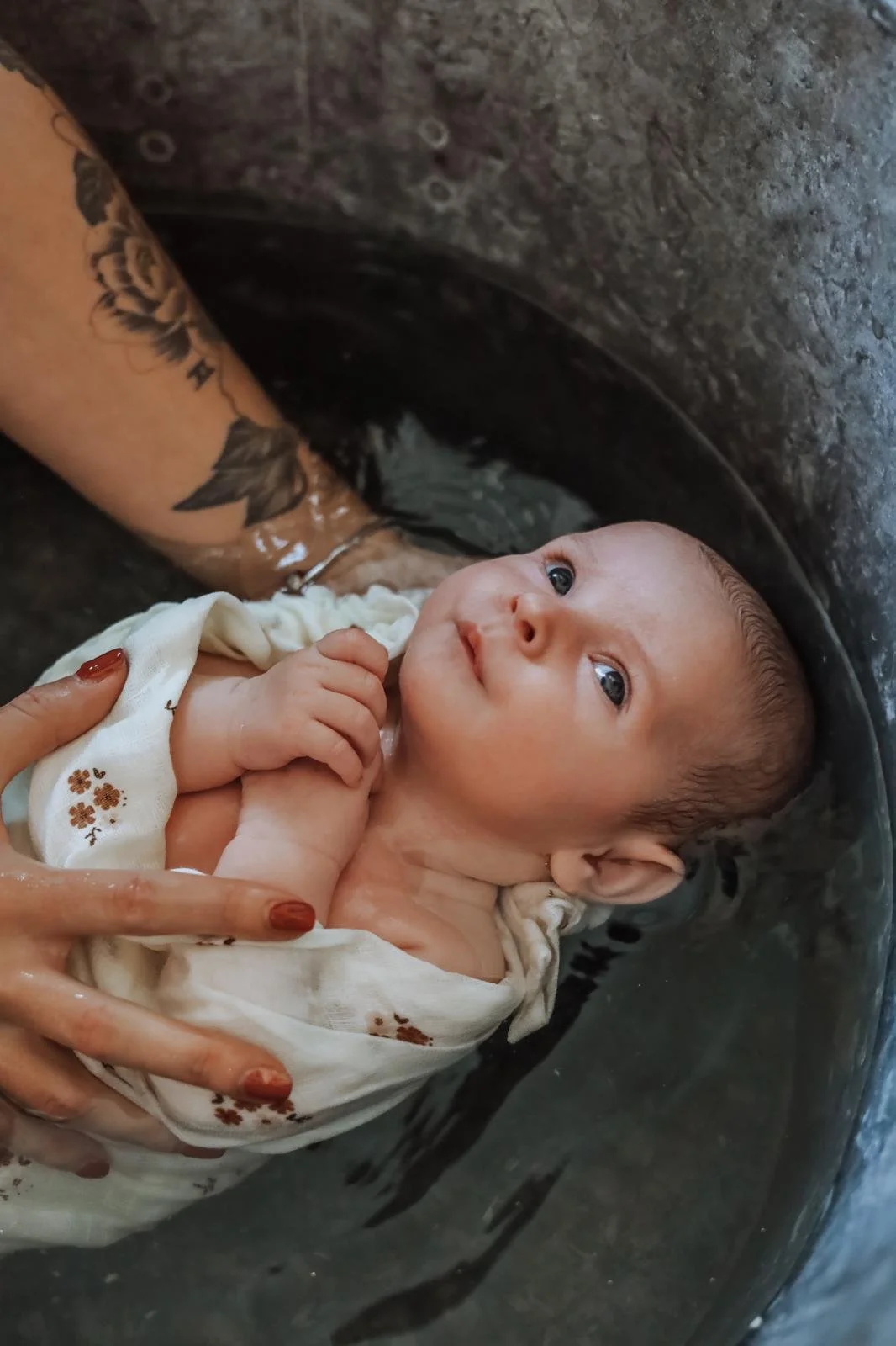Un bébé en train d'être baptisé dans une bassine avec de l'eau, une personne le tient doucement.