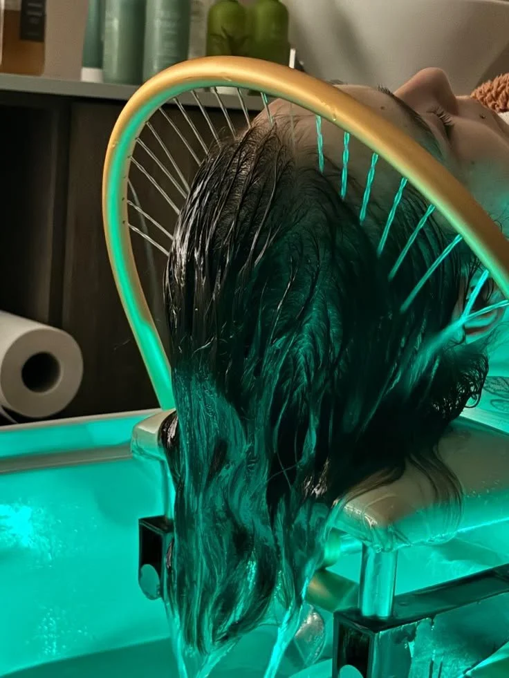 Une personne reçoit un traitement de lumothérapie capillaire dans un centre spécialisé, avec des lumières LED vertes et un appareil de soins capillaires.