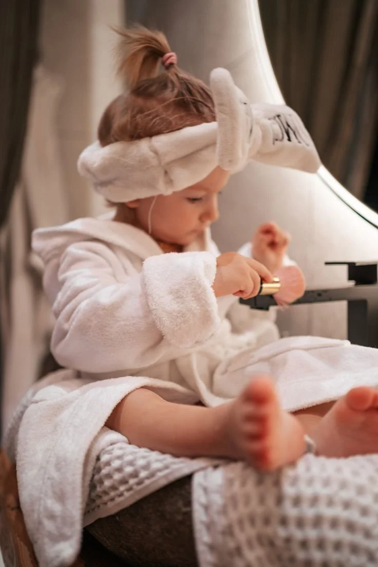 Jeune fille avec une tresse portant une couronne de serviettes, assise près d'une table de nuit en soie, jouant avec un objet doré.
