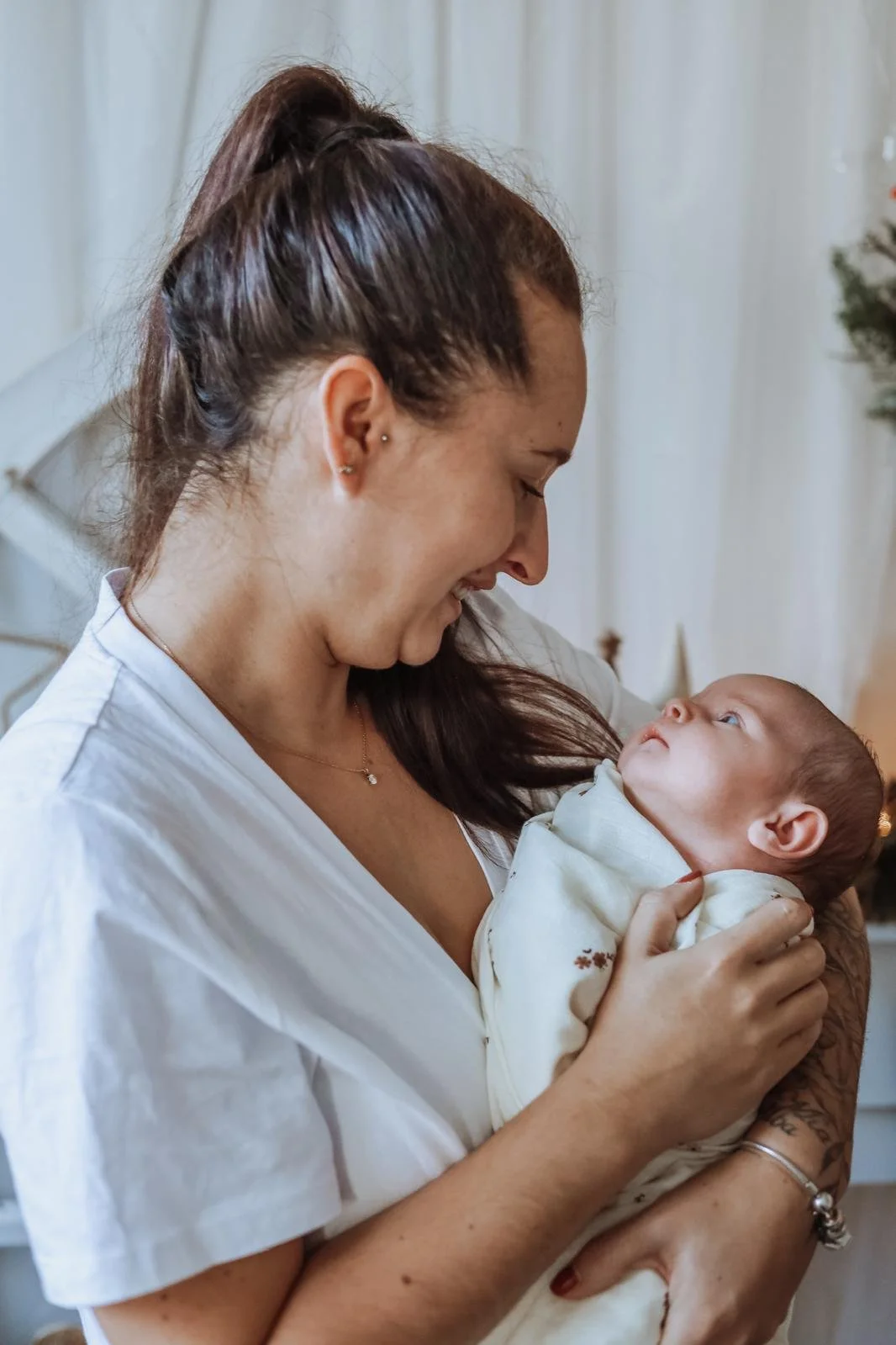 Une femme souriante tient un bébé dans ses bras, dans une atmosphère chaleureuse et lumineuse.