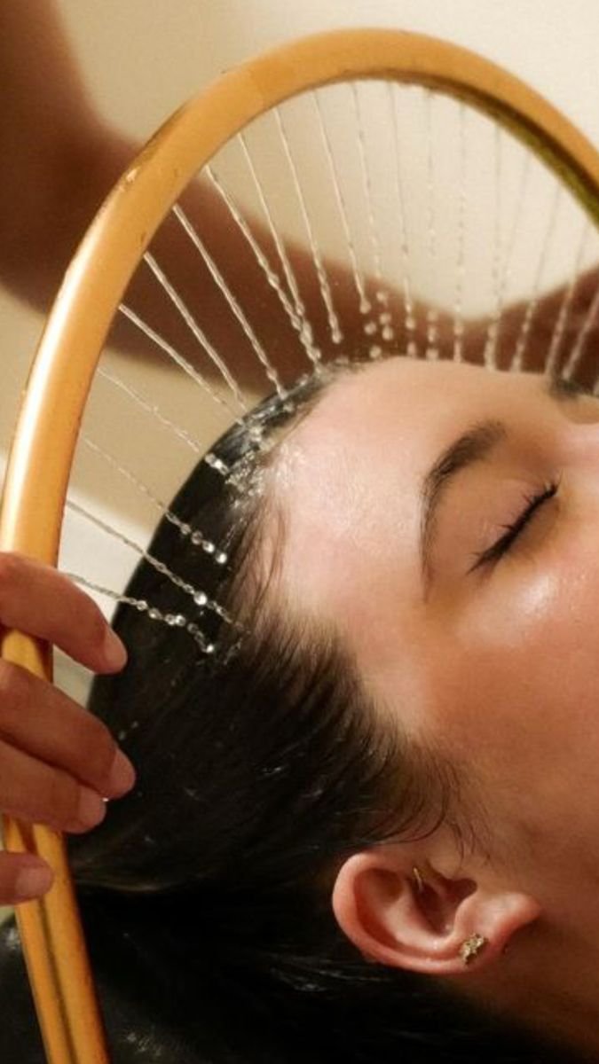 Une personne qui se lave les cheveux avec un miroir rond, éclaboussures d'eau visibles sur le miroir.