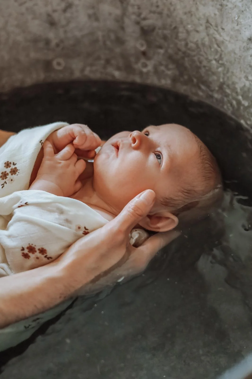 Un bébé en train d'être baptisé dans une bassine d'eau, tenu par une personne