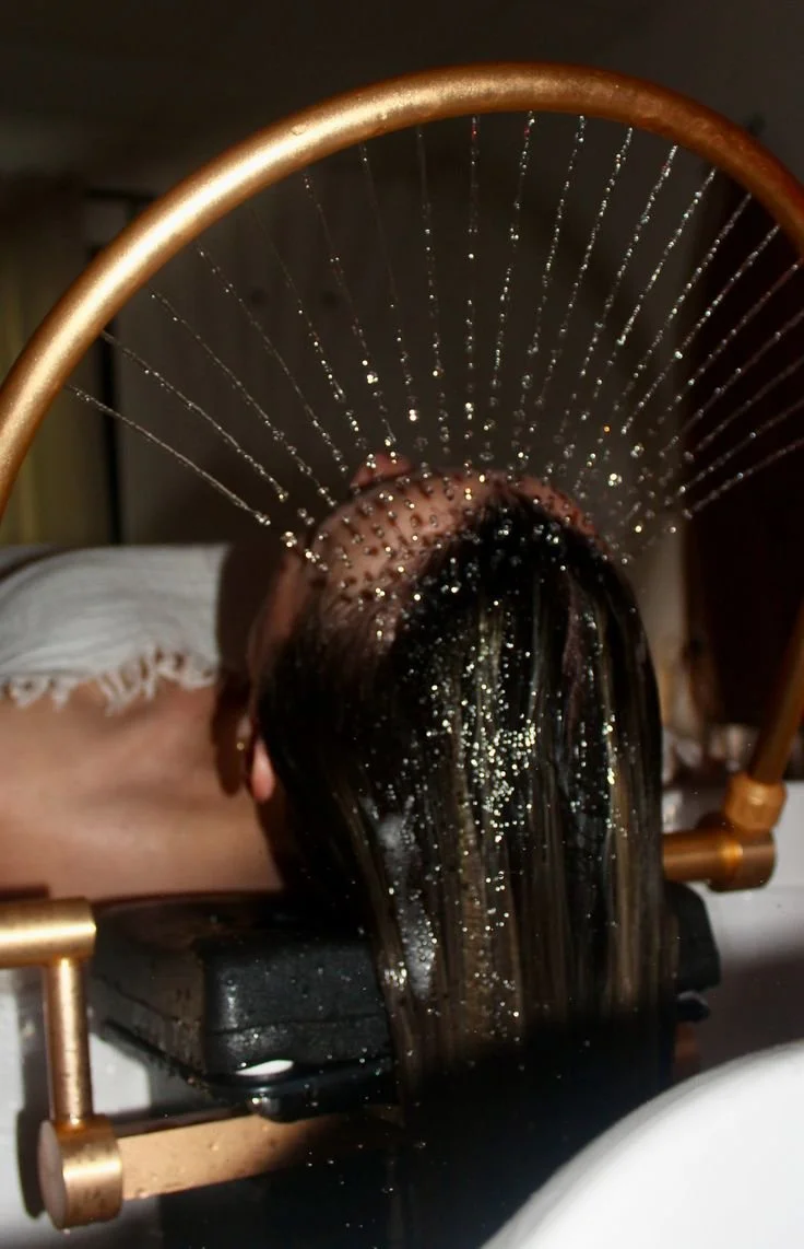 Une personne reçoit un traitement de cheveux ou un soin capillaire avec une machine qui projette une substance scintillante sur sa tête, vue de derrière.
