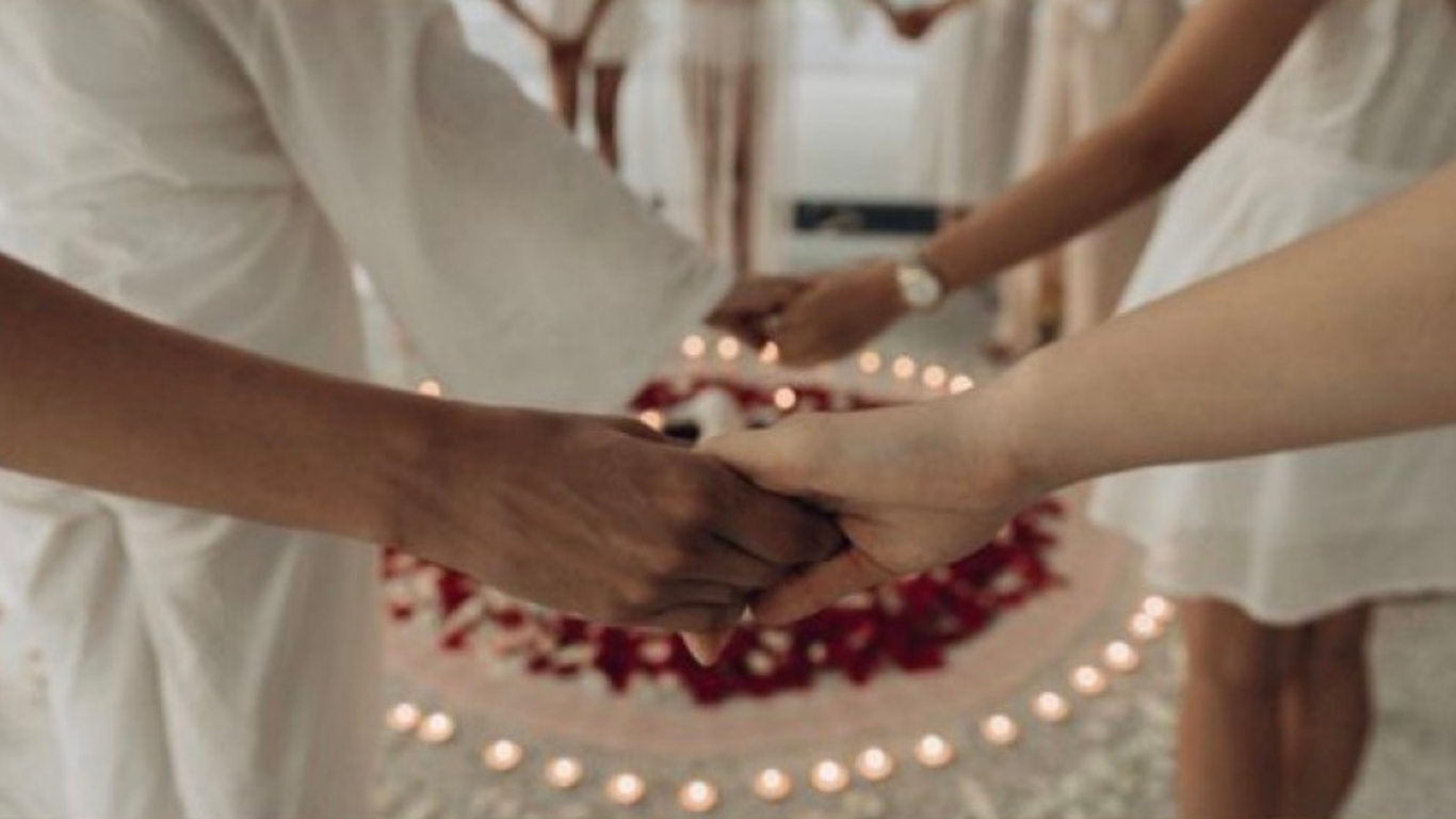 Deux personnes se tiennent la main lors d'une cérémonie, entourées de bougies et de décorations florales.