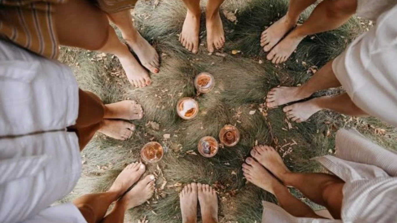 Six personnes pieds nus, formant un cercle autour de plusieurs bougies, vu d'en haut, dans un environnement extérieur avec de l'herbe et des feuilles. Le cercle médecine.