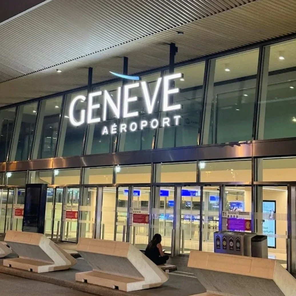 Entrée principale de l'aéroport de Genève illuminée de nuit, avec l'enseigne Genève Aéroport visible en façade