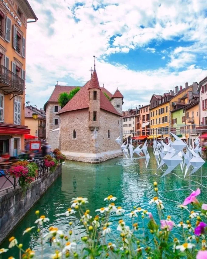 canaux du vieil Annecy en été, avec façades colorées, fleurs et sculptures origami flottant sur l'eau