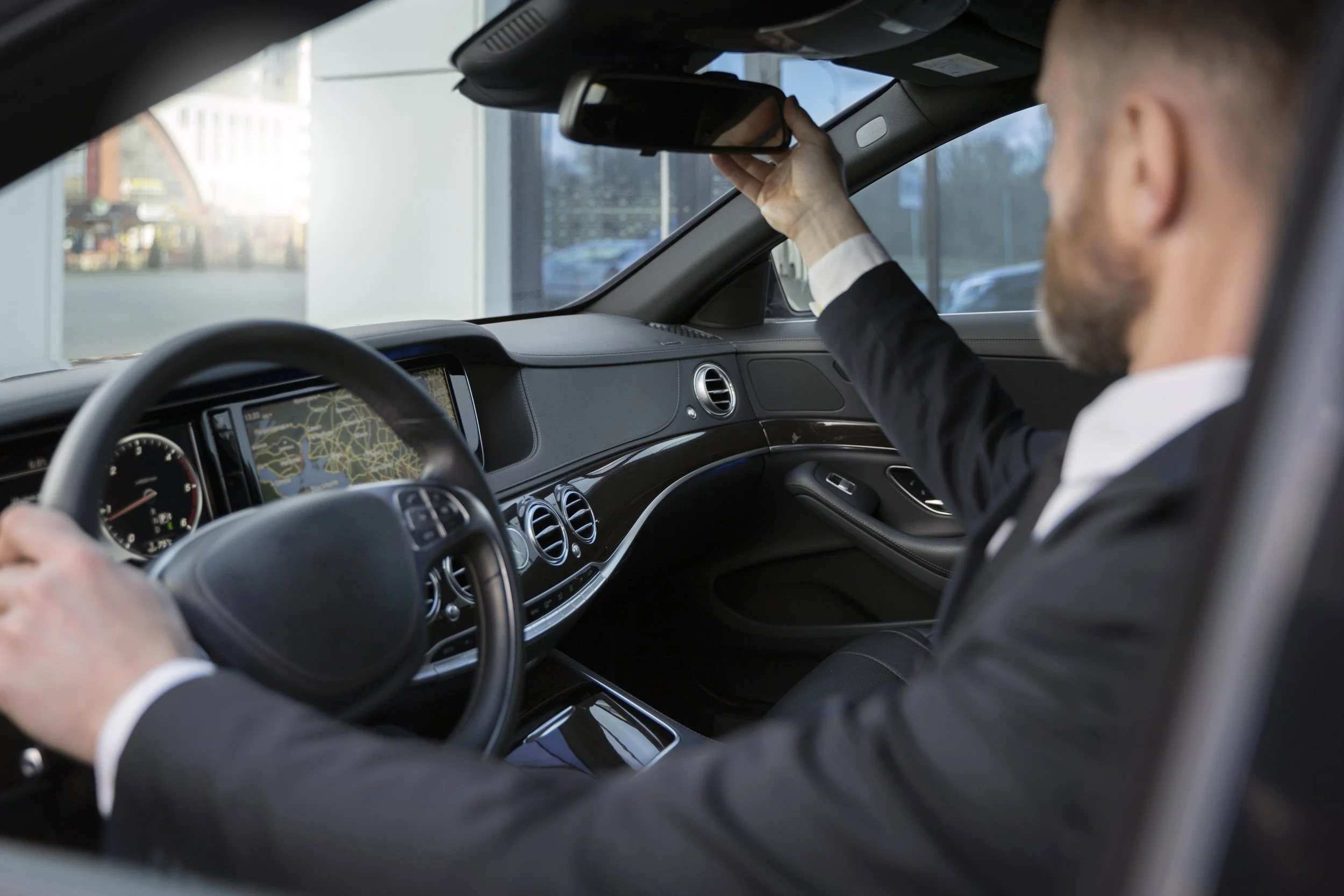 Chauffeur professionnel en costume au volant d'un véhicule de prestige, ajustant son rétroviseur intérieur