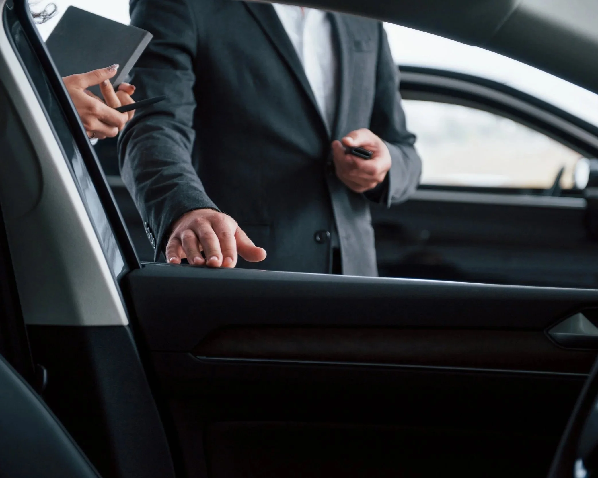 Chauffeur en costume ouvrant la portière d'un véhicule haut de gamme pour accueillir un passager, service de transport avec chauffeur
