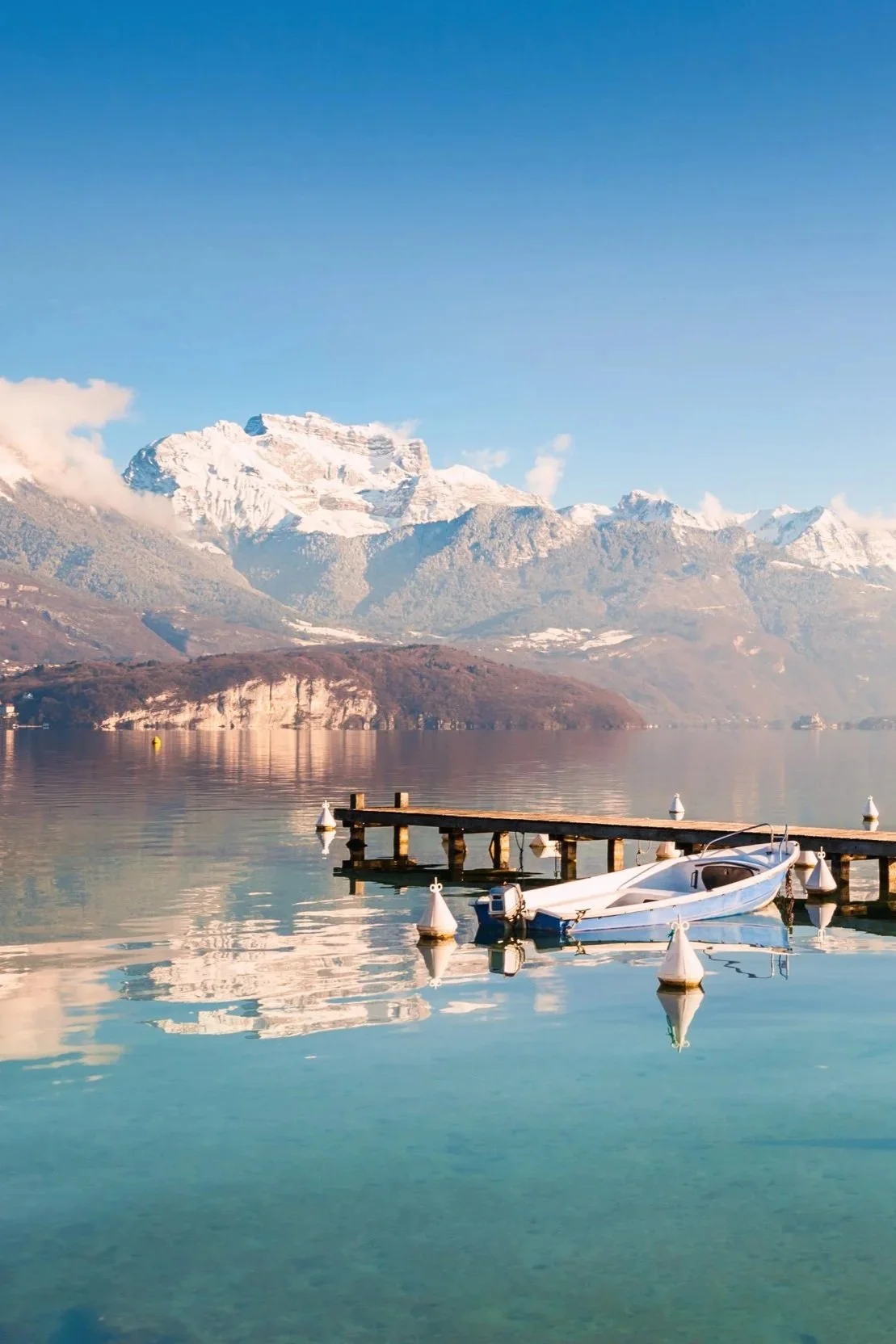 ponton en bois sur le lac d'Annecy en hiver, avec reflets des montagnes enneigées
