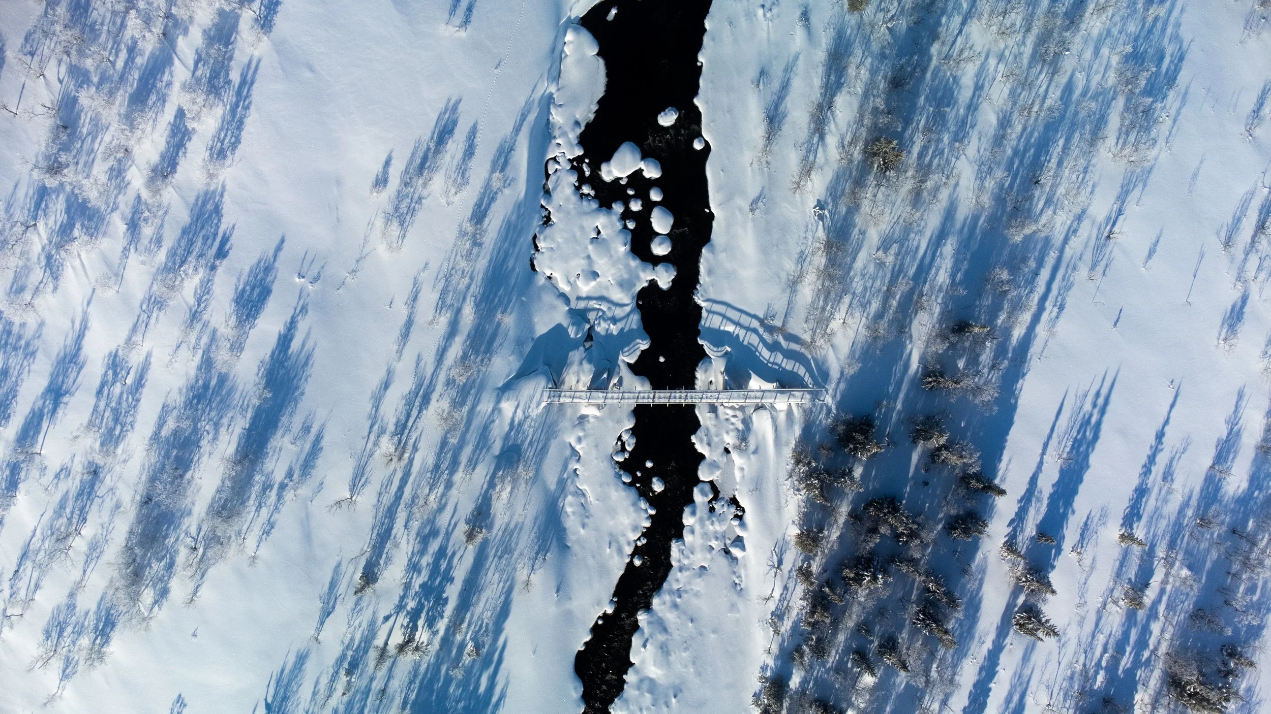 Aerial view of a snow-covered landscape with a narrow black river running through it, surrounded by snow and trees. Iced lake in Sweden, dji

