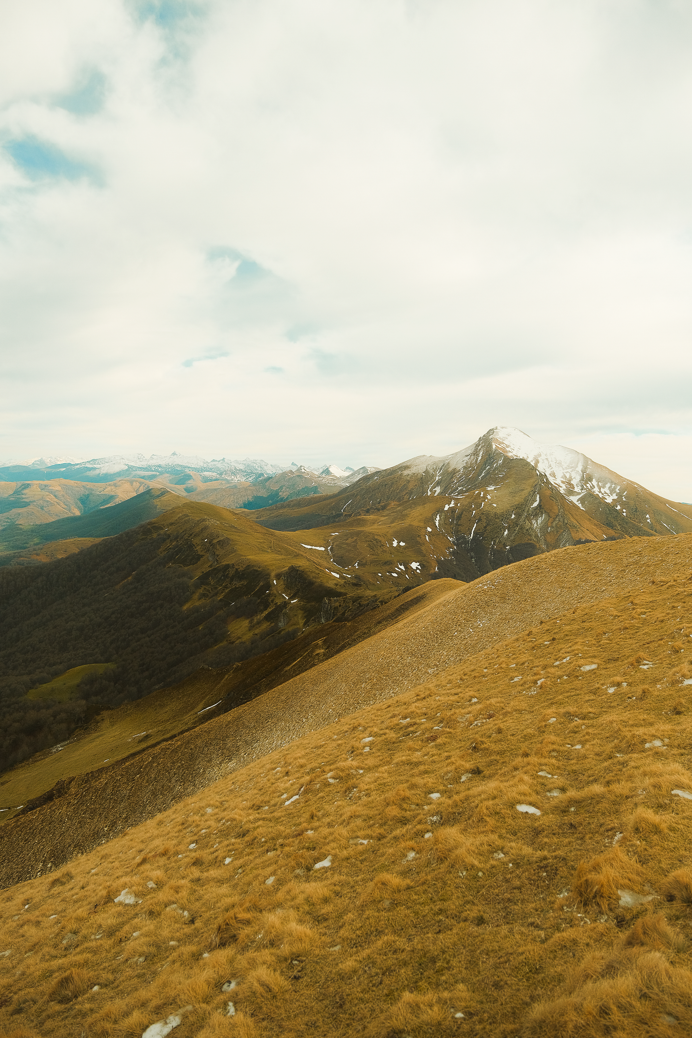 Mountain landscape with snow-capped peaks, rolling hills, and grassy slopes under a partly cloudy sky. Iraty, x-t4

