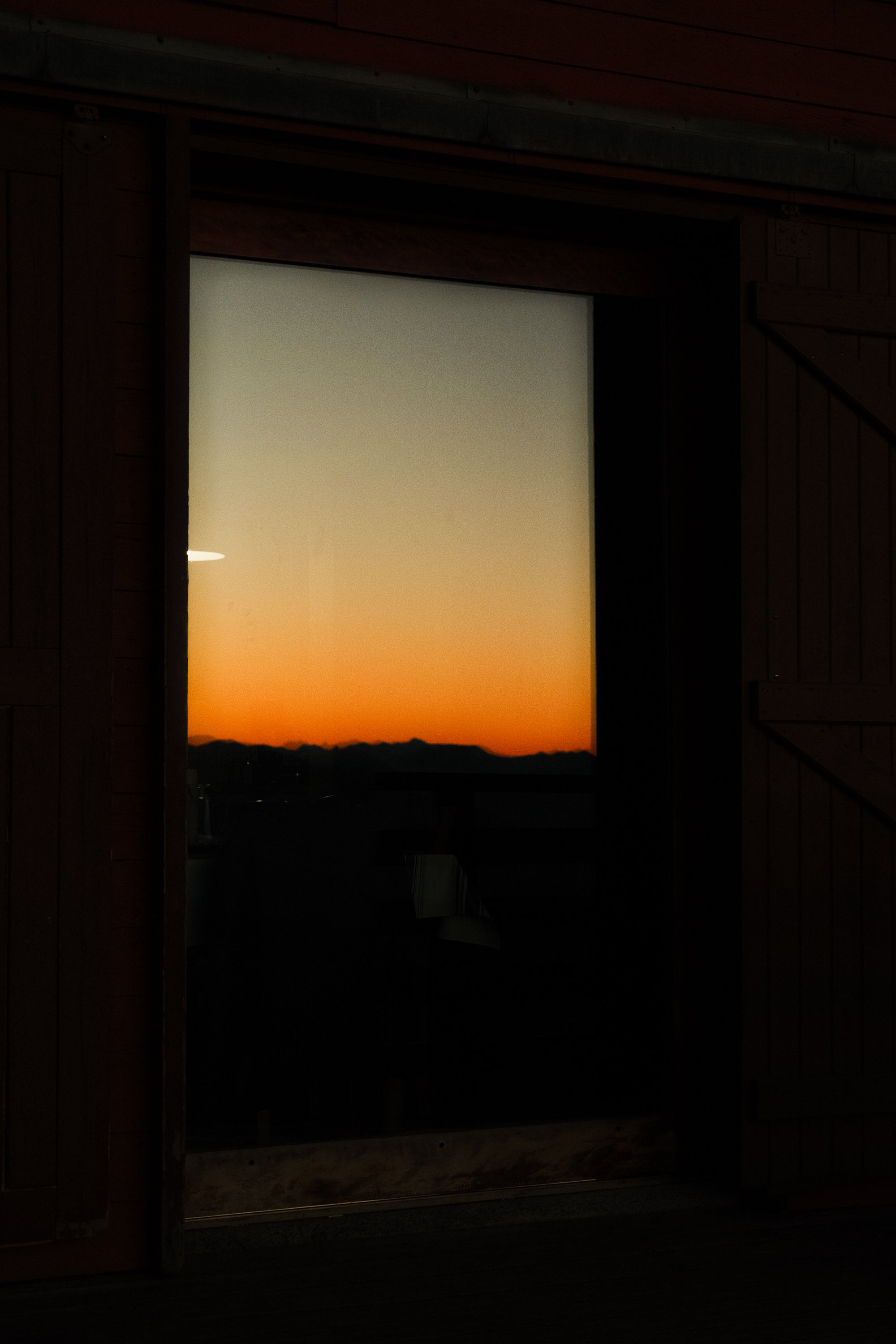 Looking through a barn door window at a sunset over mountains. Night in Iraty