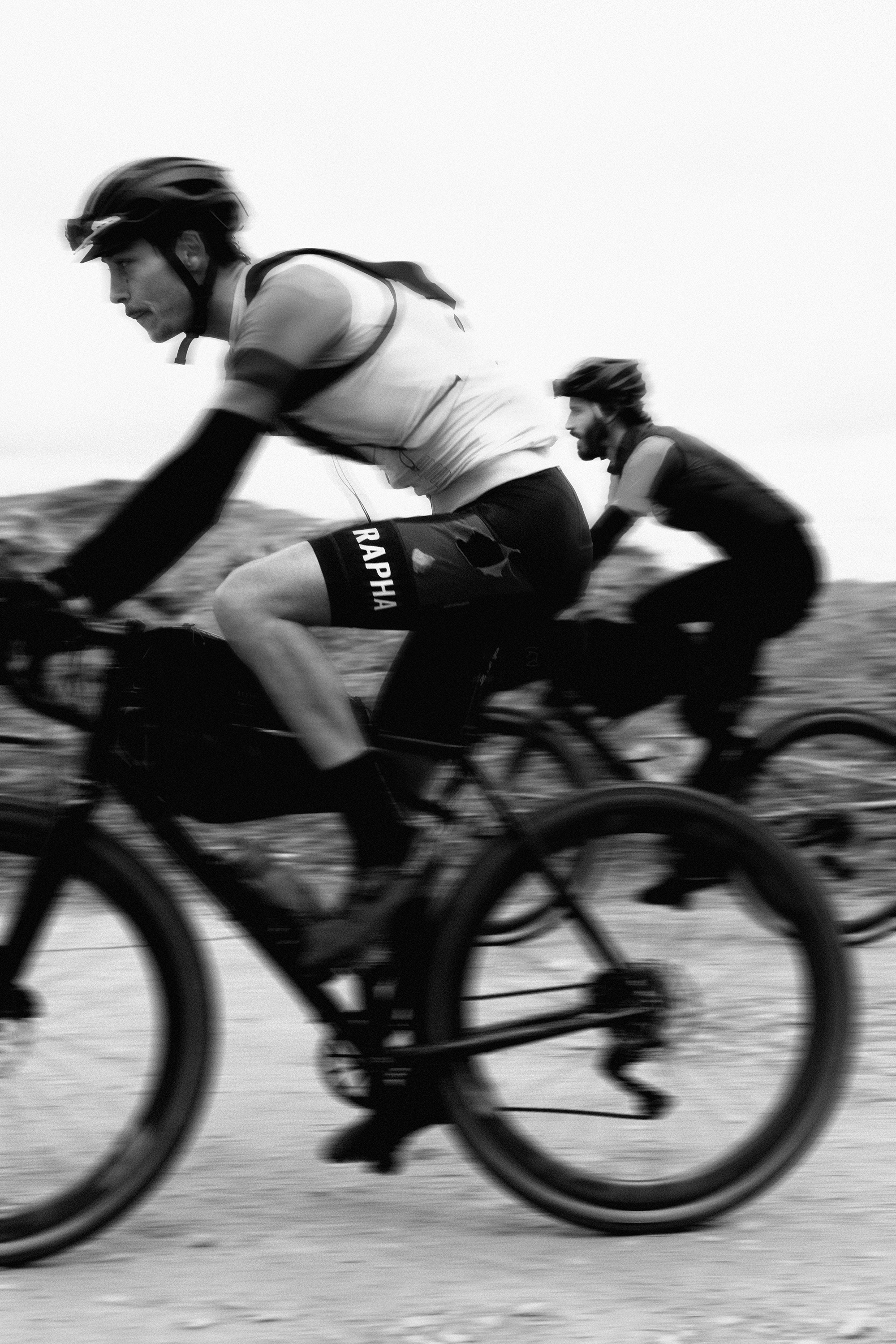 Two cyclists riding mountain bikes on a trail, wearing helmets and athletic clothing, with a blurred background indicating motion at FlatLands race.
