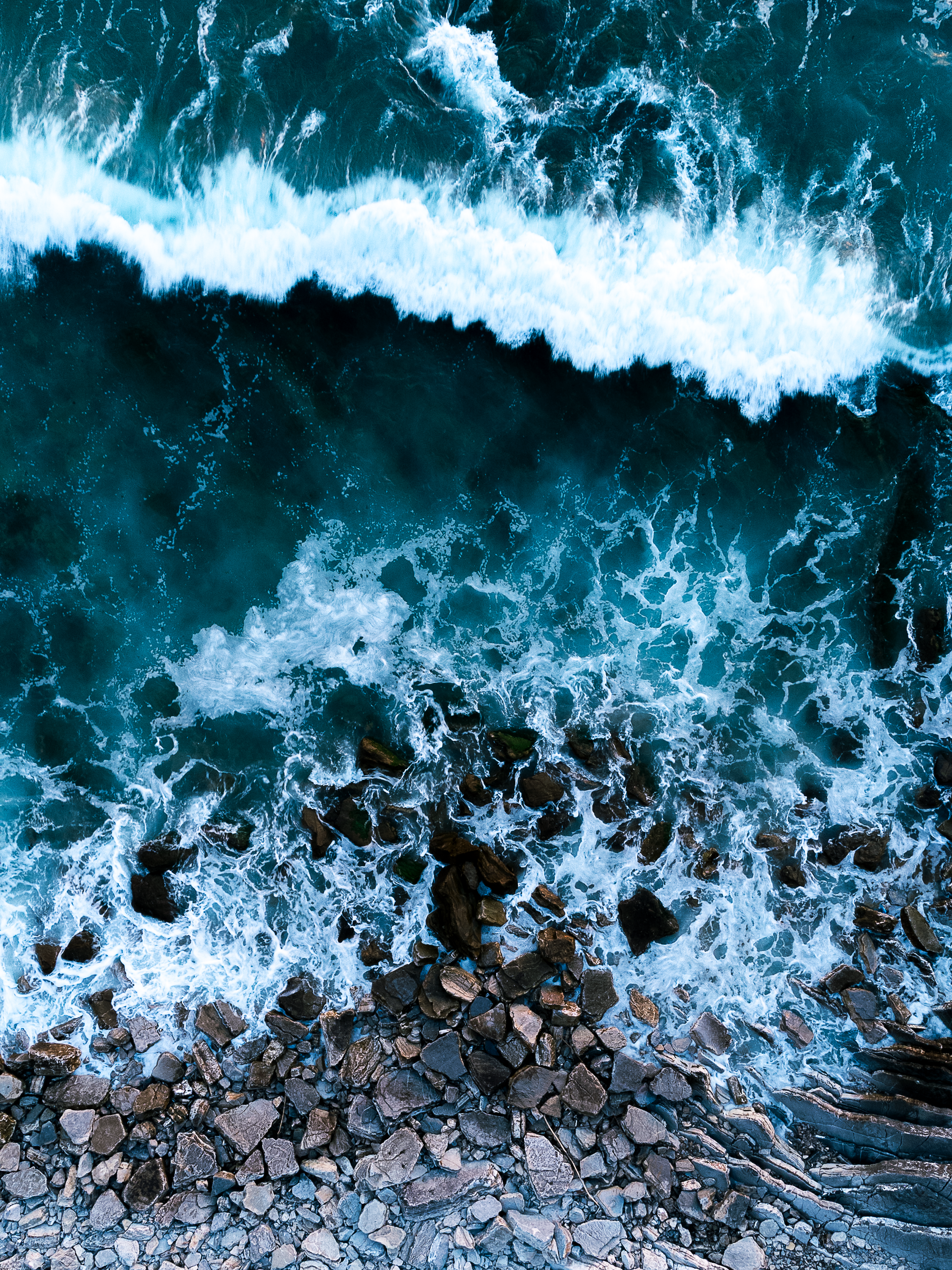 Aerial view of ocean waves crashing over rocks along a rocky shoreline. Localized in Erromardie
