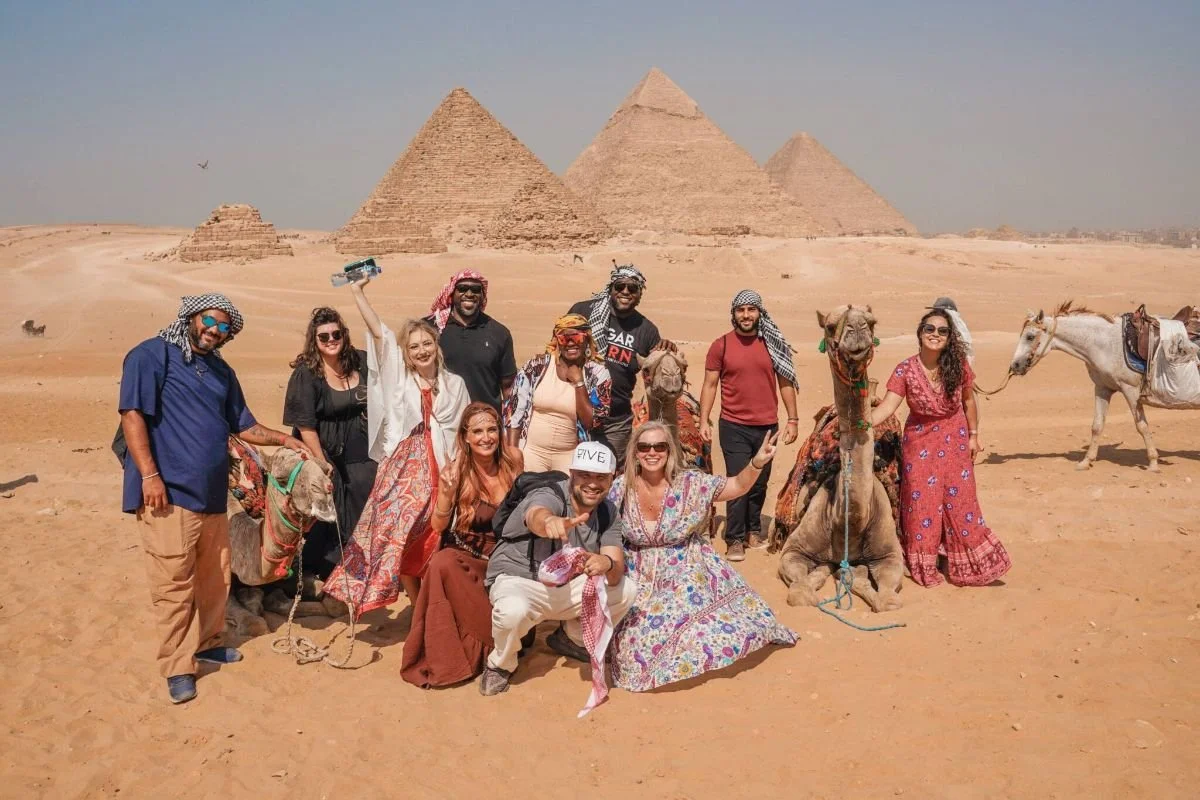 VIVE Society Group Tours to Egypt. Group of travelers posing with camels at the pyramids.