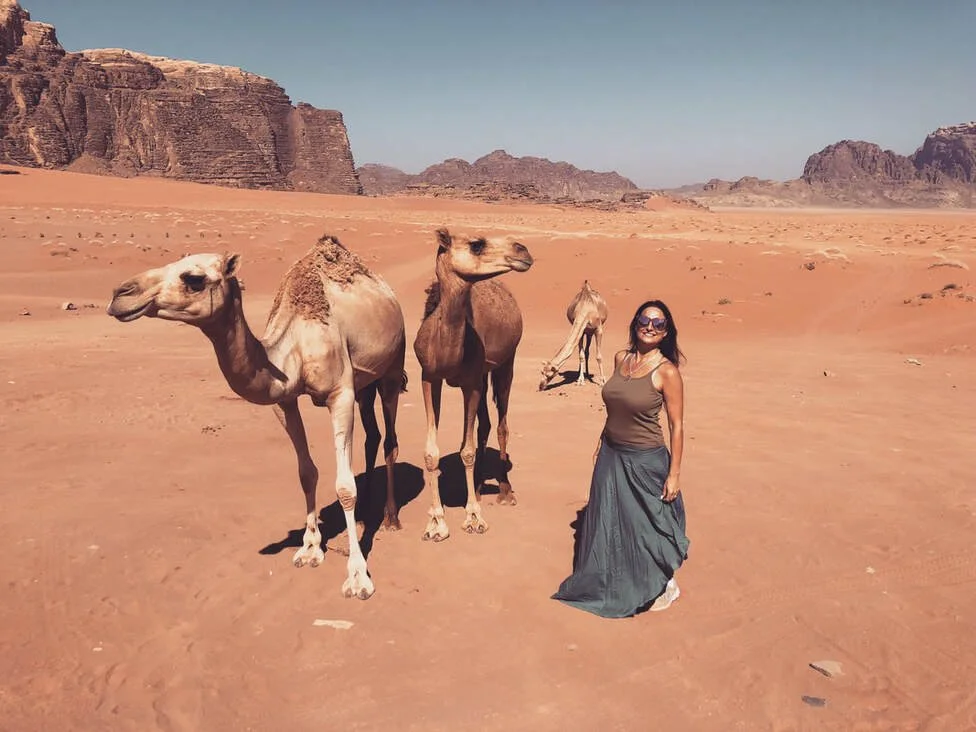 Michelle Ruiz standing with wild baby camels in Wadi Rum Desert, Jordan