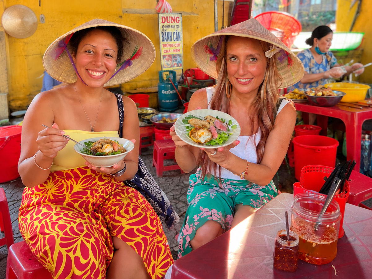 2 ladies trying pho soup on plastic stools in Hoi An Vietnam
