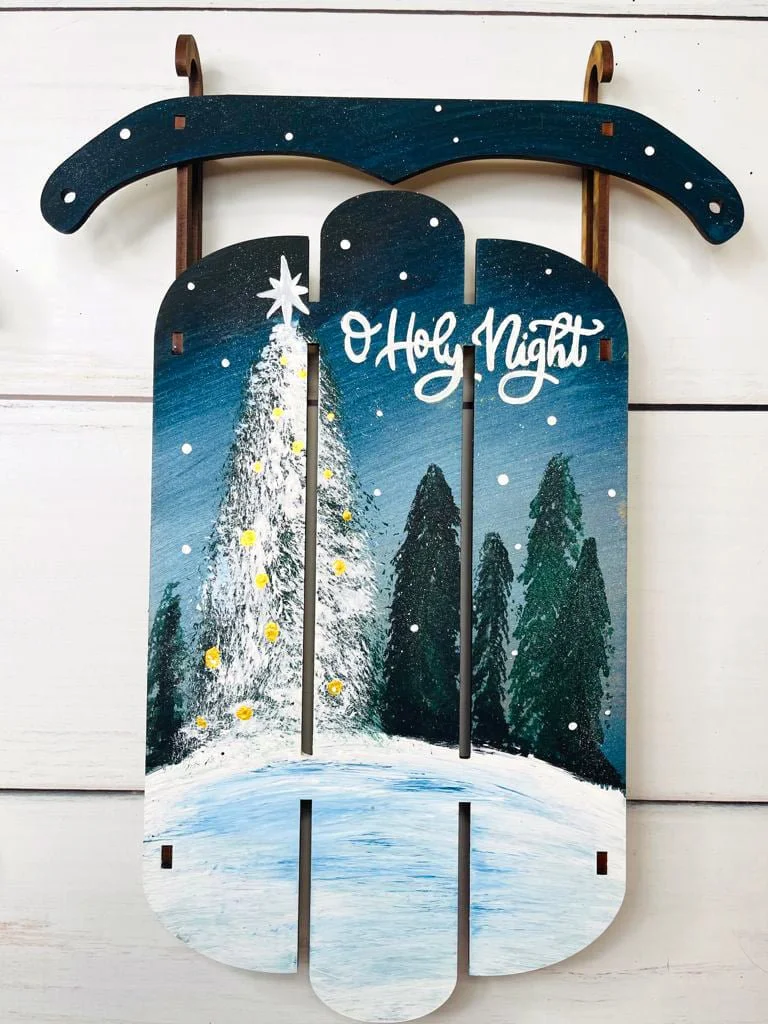 Painted wooden wall decor with a Christmas tree, snowy landscape, pine trees, and the phrase 'O Holy Night' in white script.