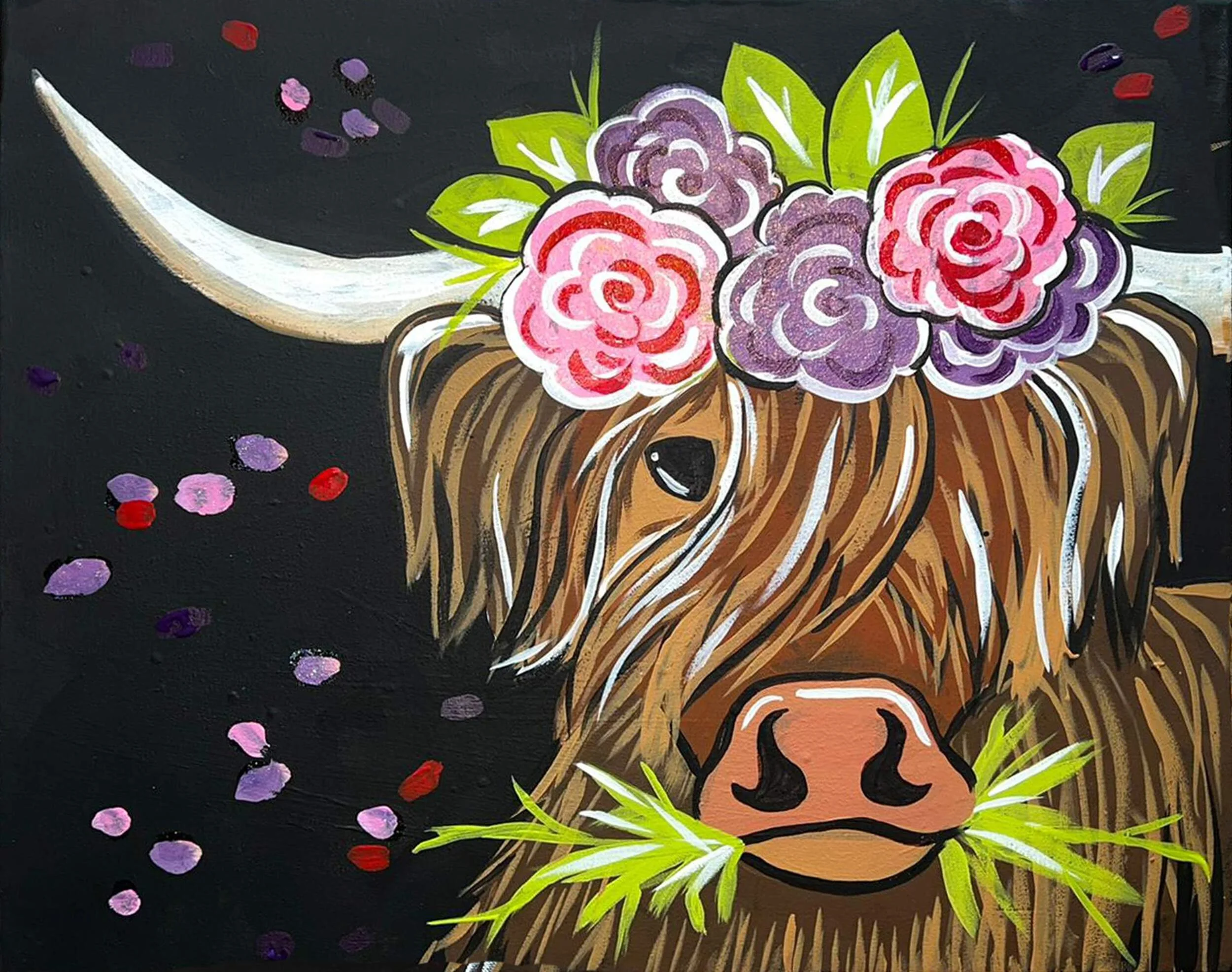Painting of a Highland cow with long hair, adorned with pink and purple flowers on the head and green leaves. The cow has a pink nose, black eyes, and is holding green grass in its mouth. The background is black with scattered purple, pink, and red spots.