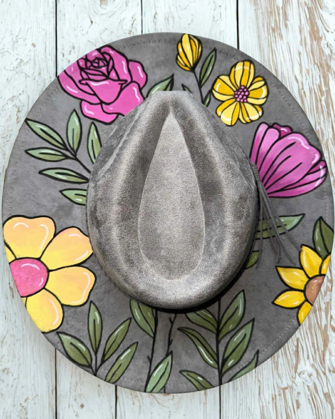 A gray felt fedora hat rests on a round, gray, floral-patterned placemat on a white wooden surface.