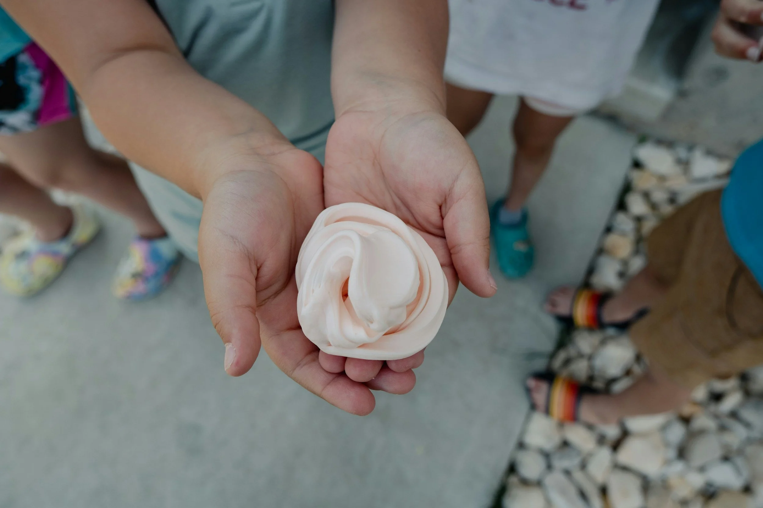 A person holding a white swirl of foam or soap in their hand, with other children standing nearby.