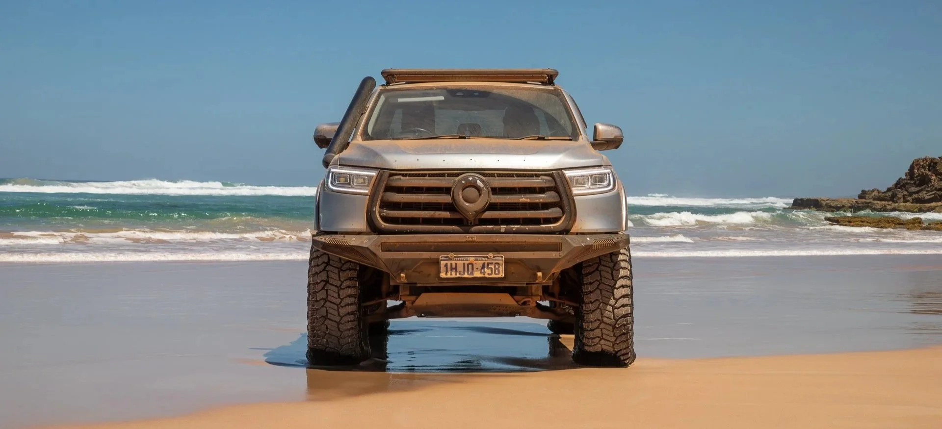 A rGWM Cannon parked on a sandy beach with ocean waves and rocky formations in the background.