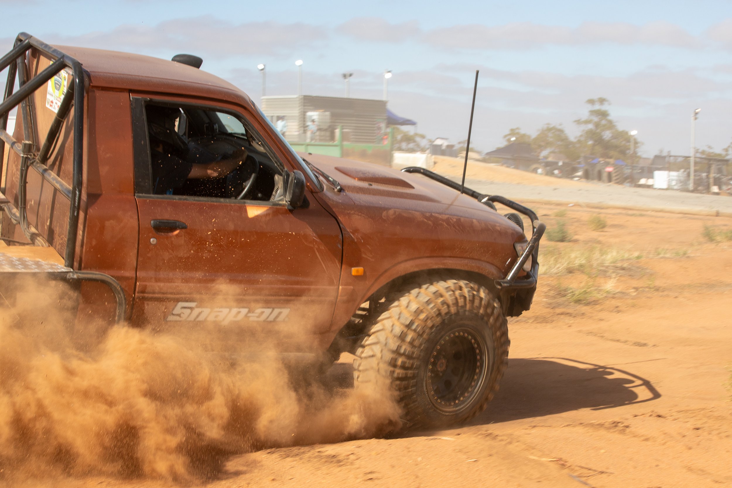 An orange 4WD kicking up dust while driving on a dirt track during daytime.