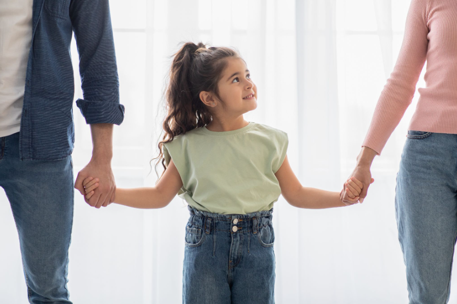 Smiling girl walking with both parents indoors after reaching a cooperative custody agreement