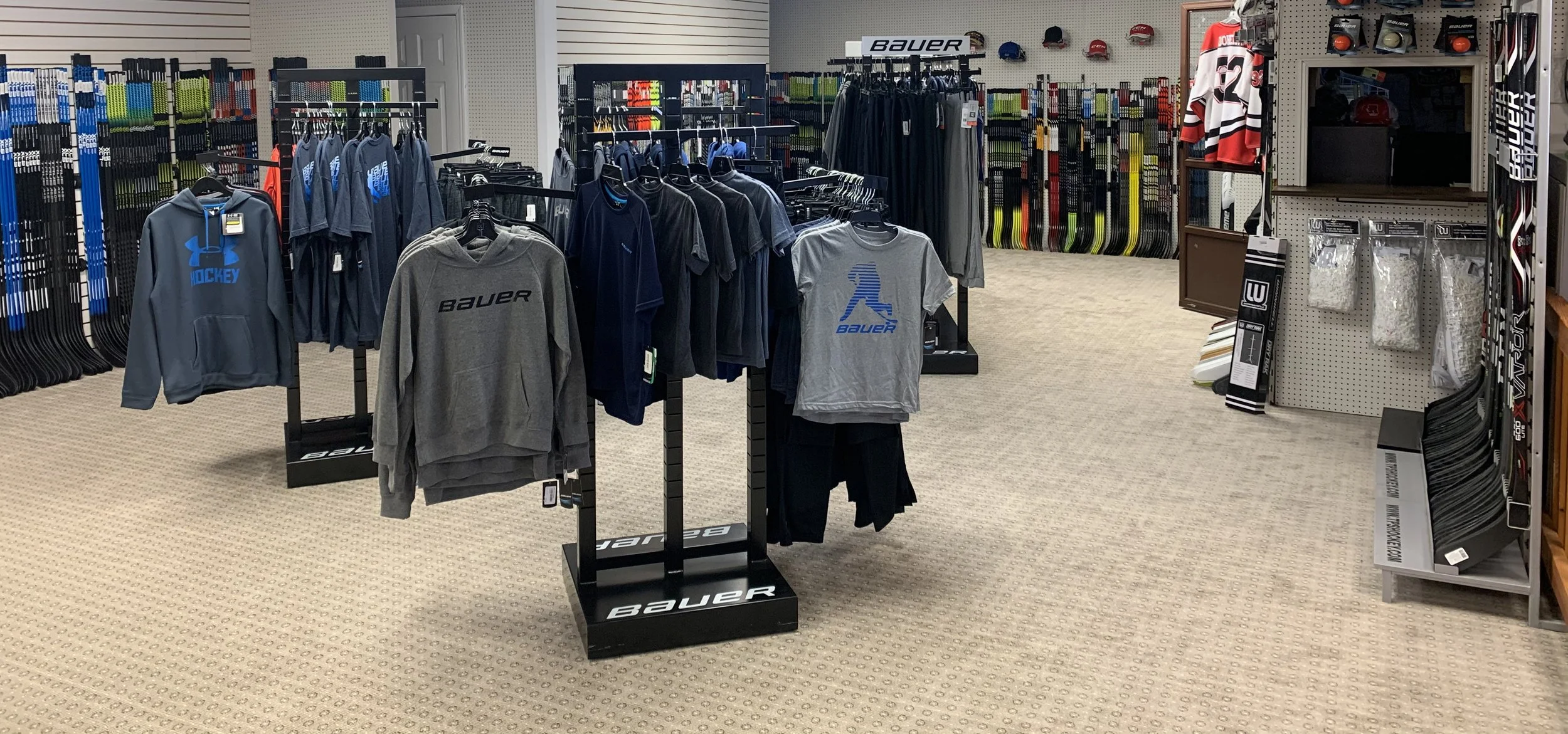 sweatshirts and tshirts on clothing racks in a store with hockey sticks in the background