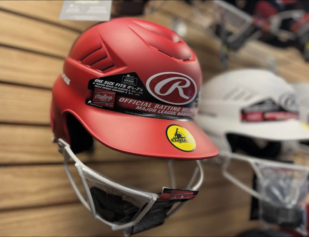 Red baseball helmet with stickers, displayed on a wooden surface.