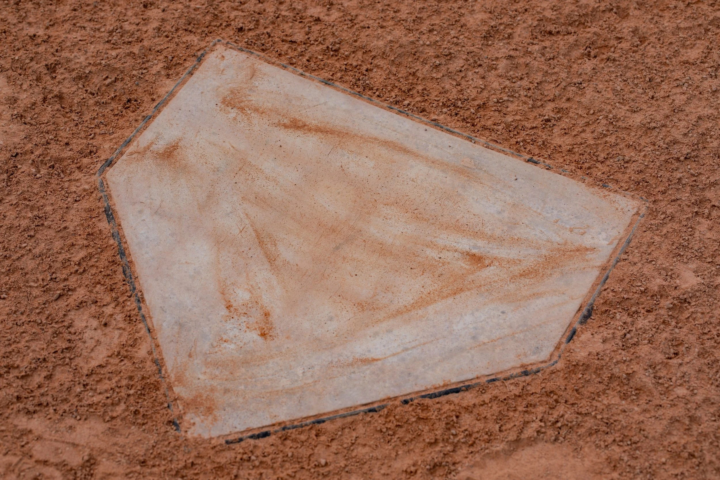 Close-up of a rectangular beige stone tile stuck in red dirt soil.