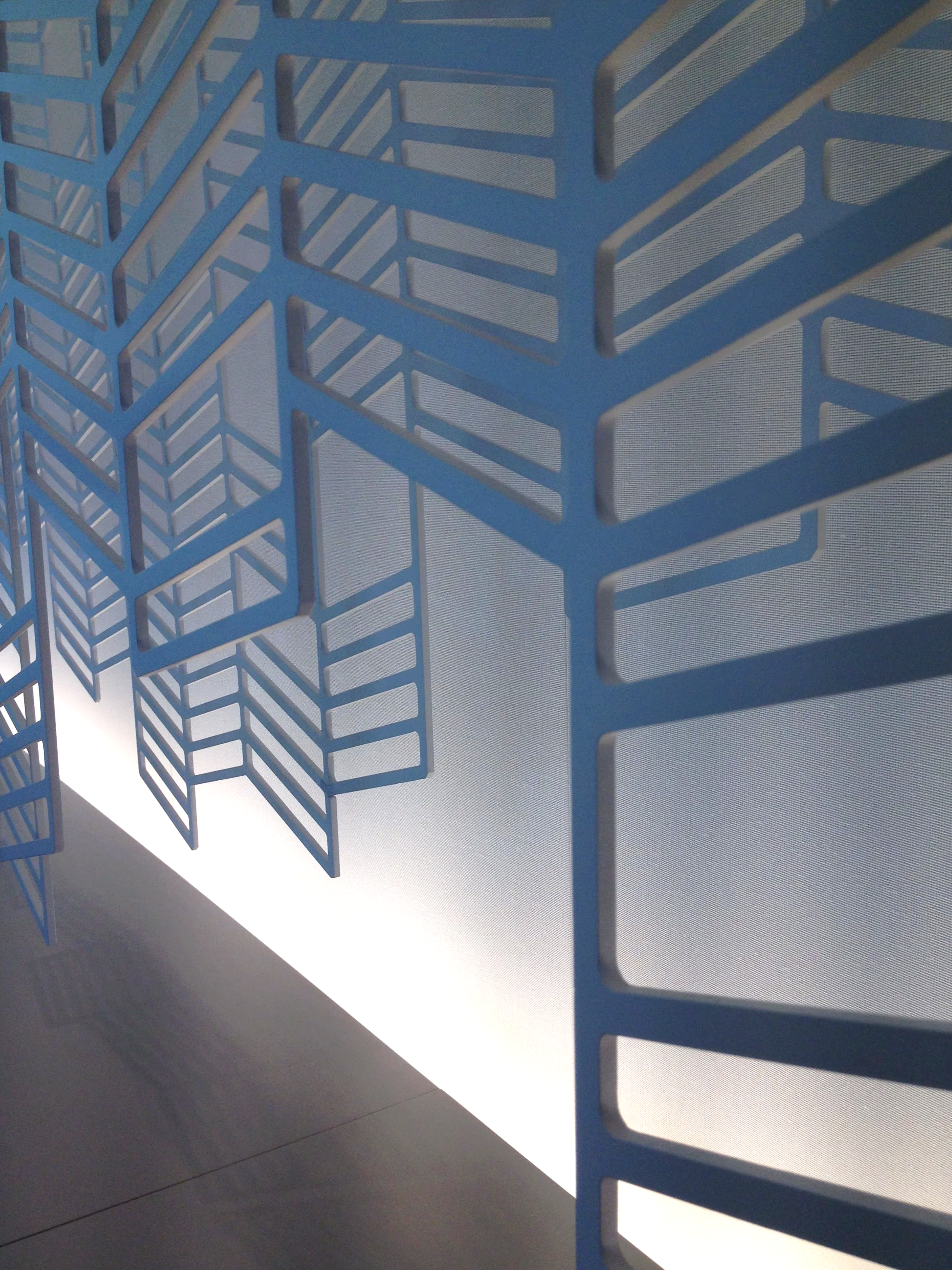 Close-up of a modern blue metal framework with geometric rectangular openings, casting shadows on a reflective surface below.