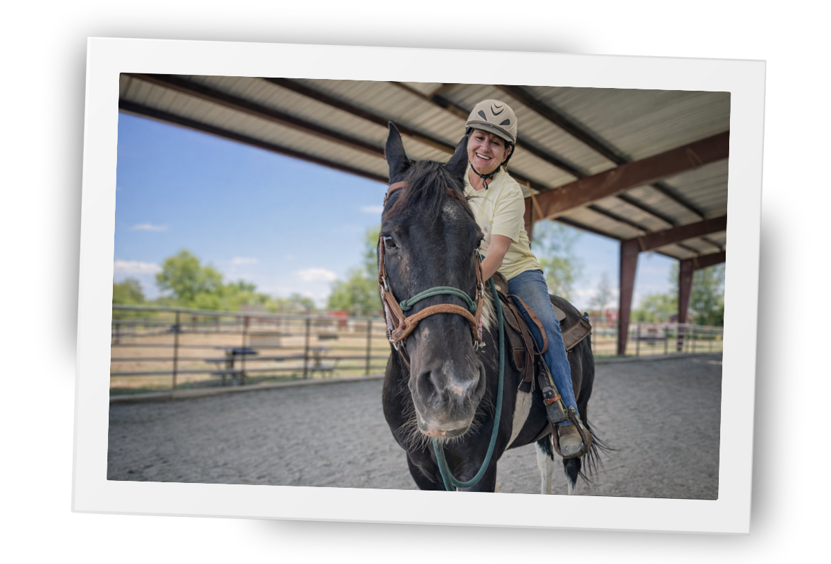 A rider participating in therapeutic riding with a calm horse in the covered arena at HorseSpeak at Cowgirl Up Ranch.