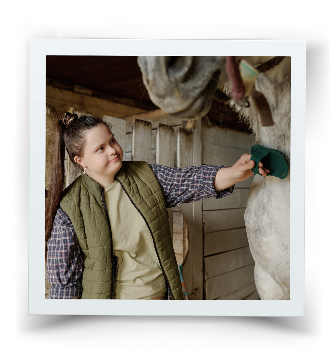 Young rider calmly grooming a horse in the barn during an adaptive riding session at HorseSpeak, showing trust, choice, and gentle connection.