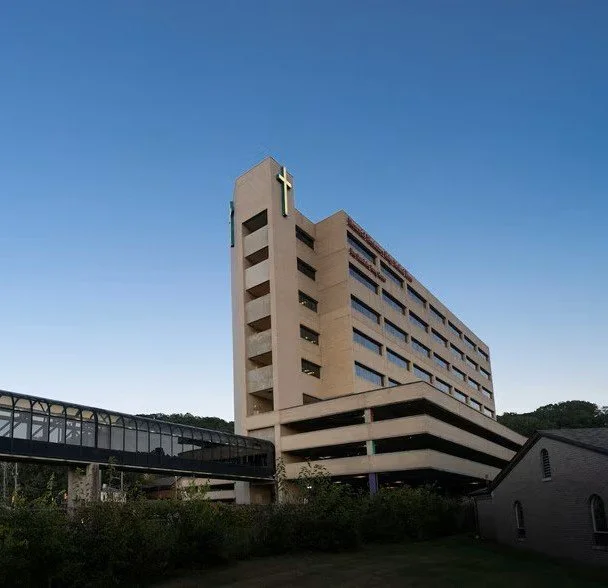 Large beige hotel building with a cross on top, connected to a glass walkway, against a clear blue sky.