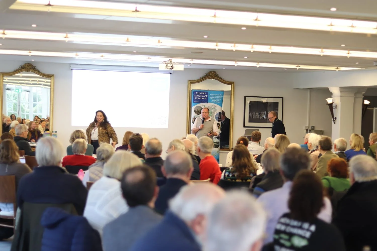large group of people facing away from the camera listening to presentations