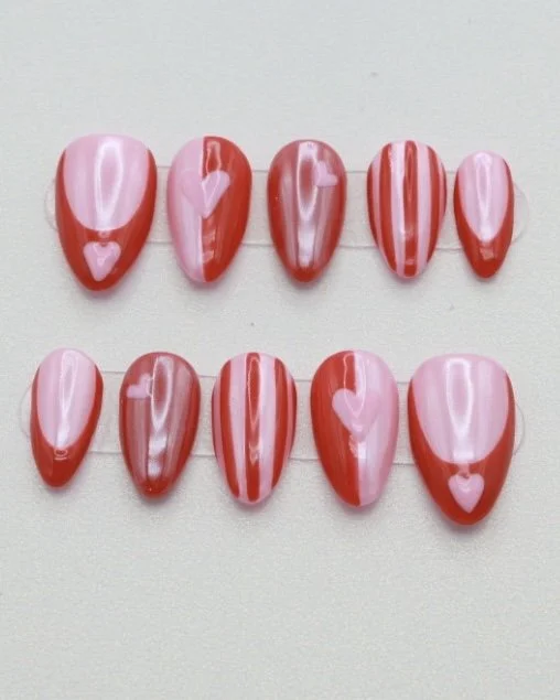 Arranged nail tips painted in pink and red with heart designs for Valentine's Day.