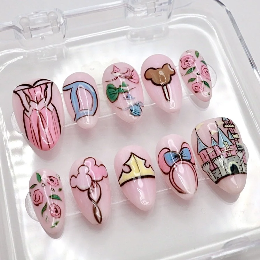 Set of 10 pink artificial nails with detailed Disney princess-themed nail art, including a castle, a pink dress, a tiara, a mouse head with a blue bow, a crown, a rose pattern, and other fairy tale elements.