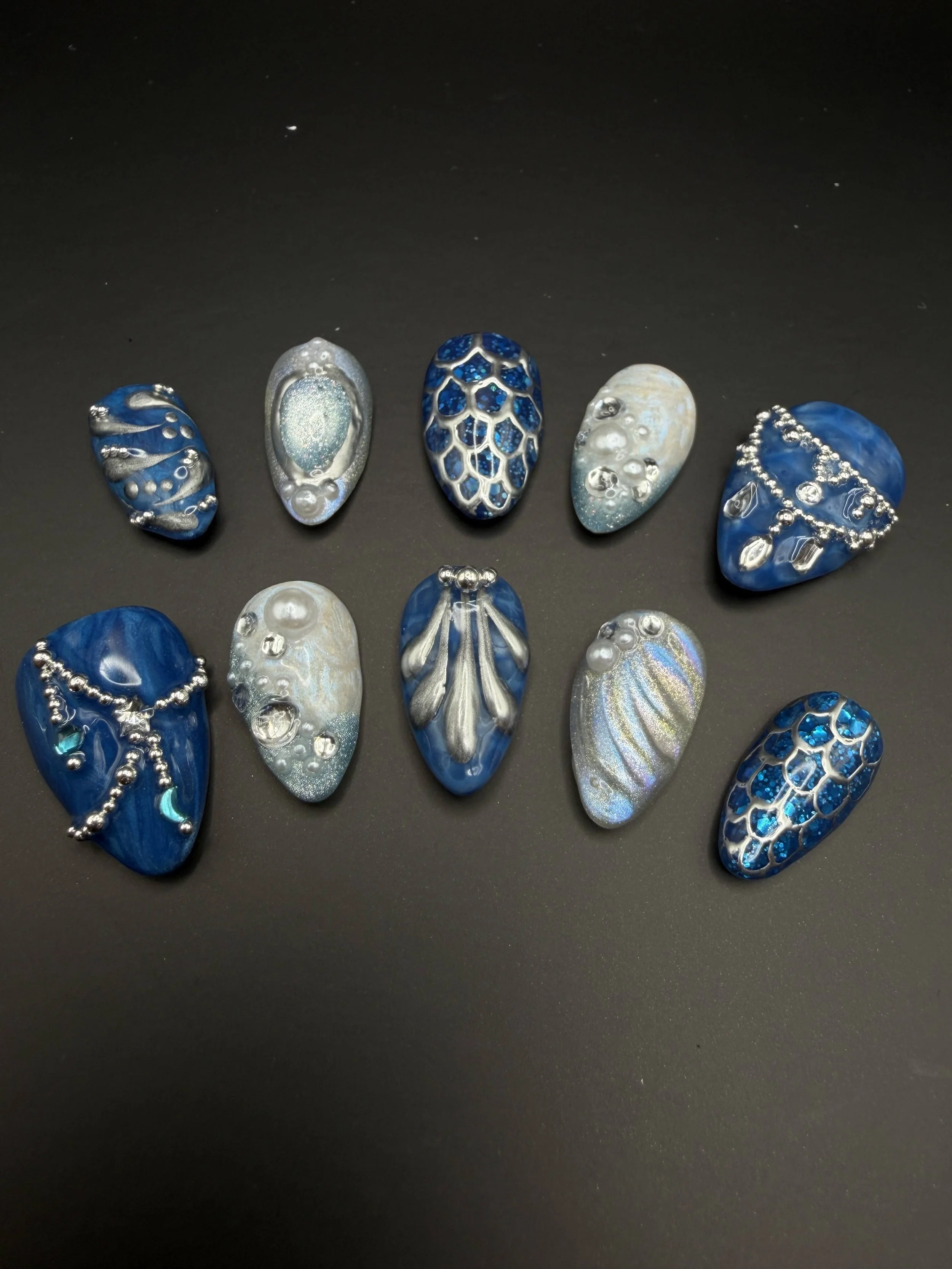 Set of ten decorative blue and silver nail art designs on black background.