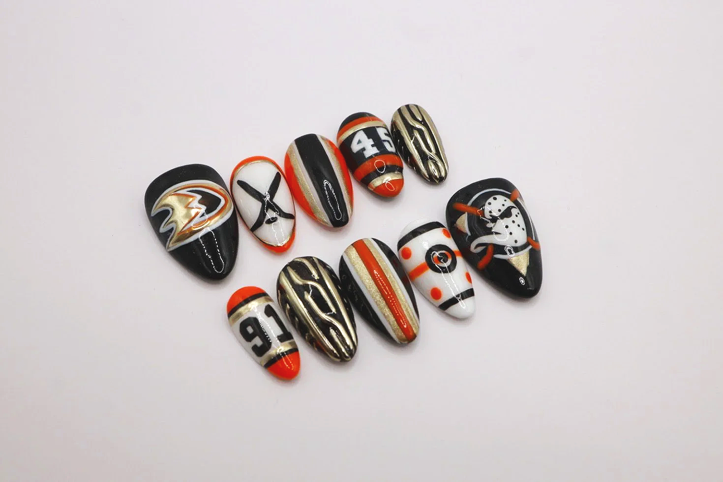 Collection of decorated football-themed nails with various designs and colors, including team logos, numbers, and patterns.