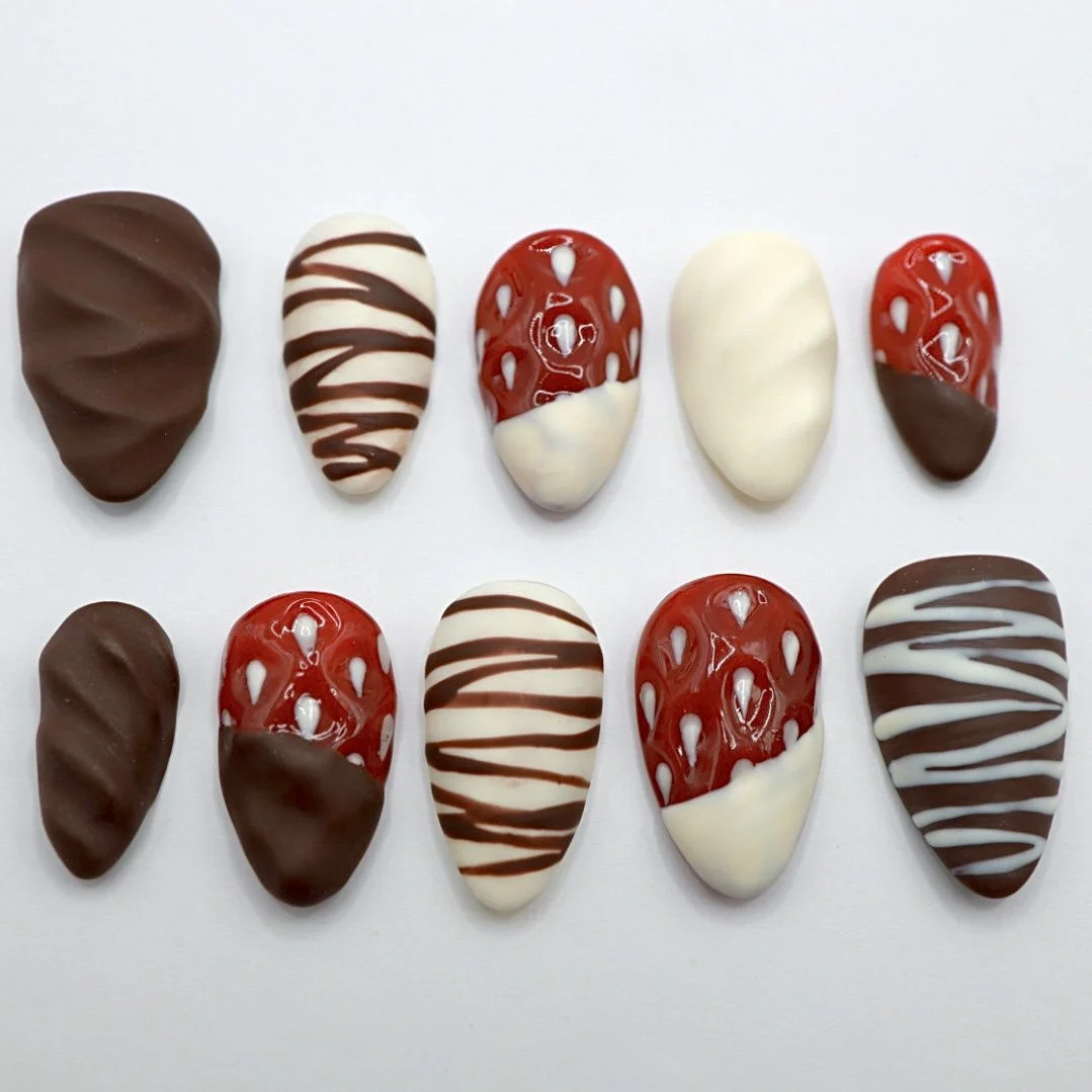 Collection of ten decorated chocolates with various patterns and colors, including white, milk, and dark chocolate, arranged in two rows on a white background.