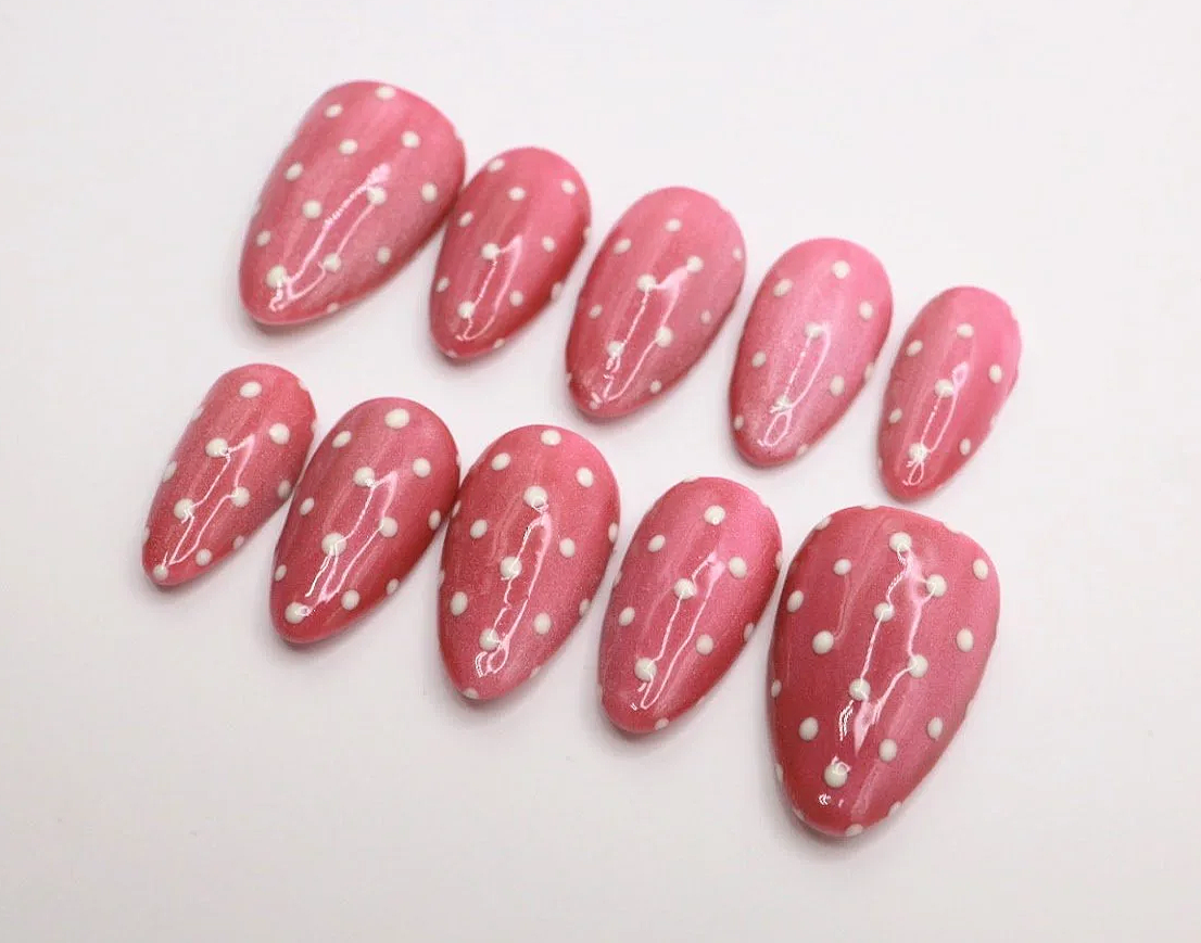 Set of ten artificial pink nails with white polka dots and white swirl designs.