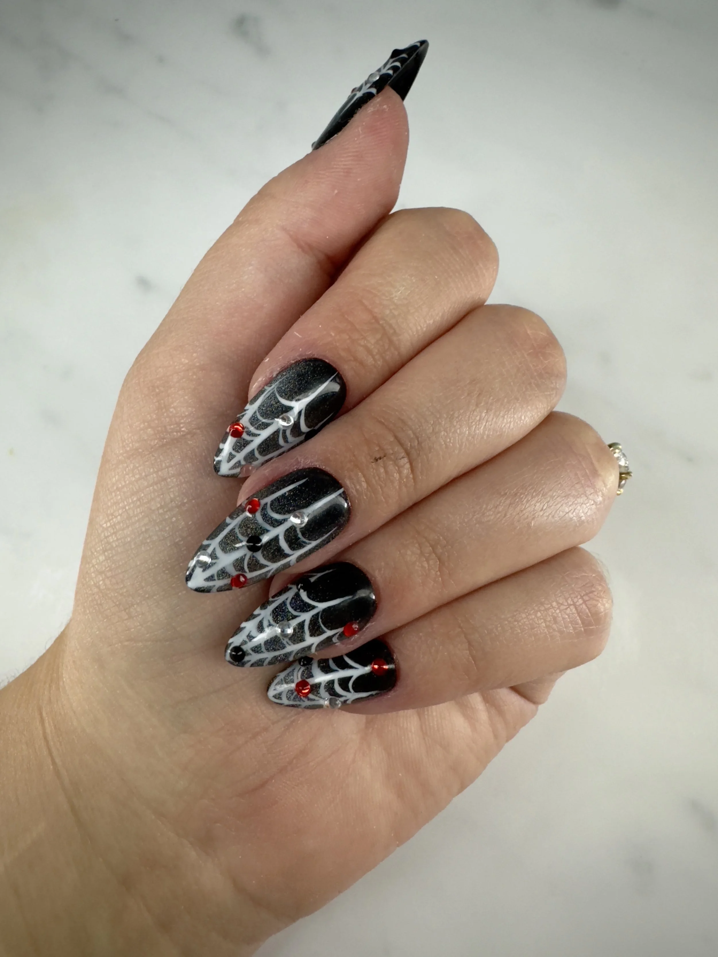 Close-up of a hand with black, white, and red spider web patterned nail art on long, pointed nails.