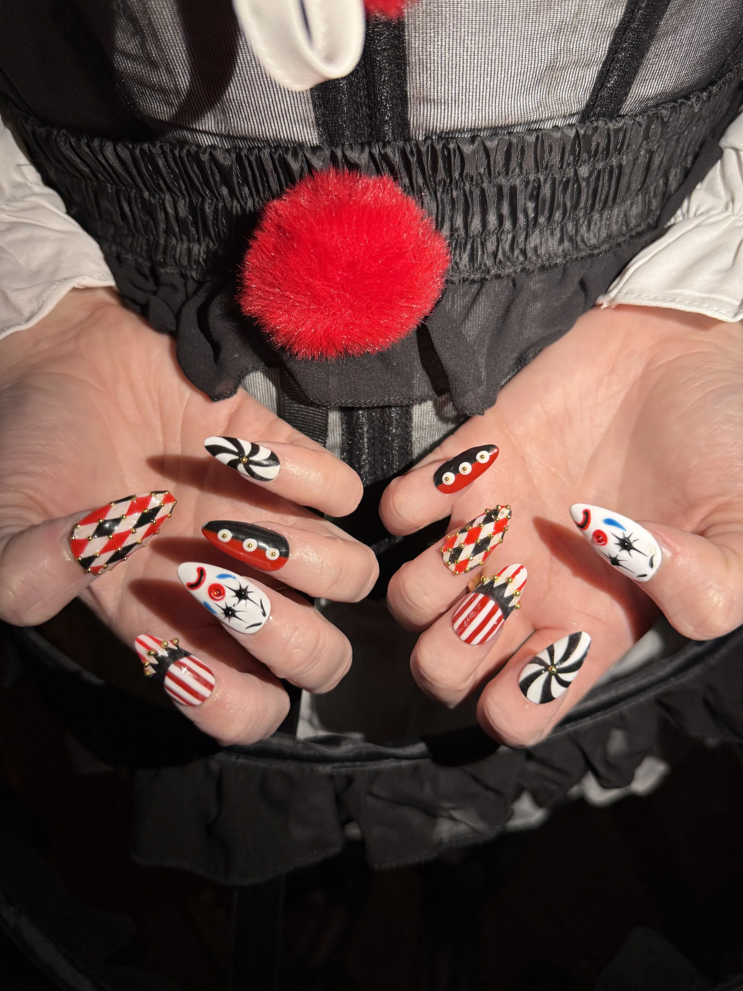 Close-up of hands with holiday-themed nail art, holding a red pom-pom, with a winter coat and snow jacket in the background.