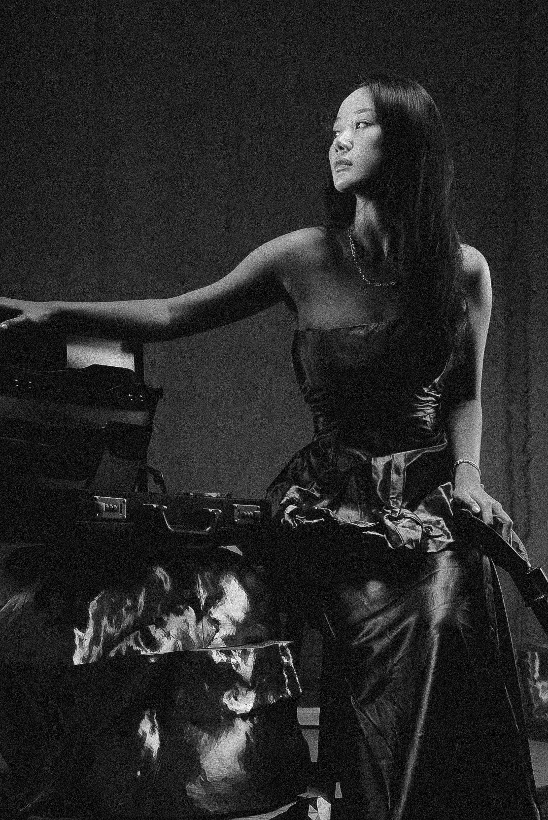 A woman with long dark hair in a strapless dress sitting on a motorcycle, looking to the side, in black and white.