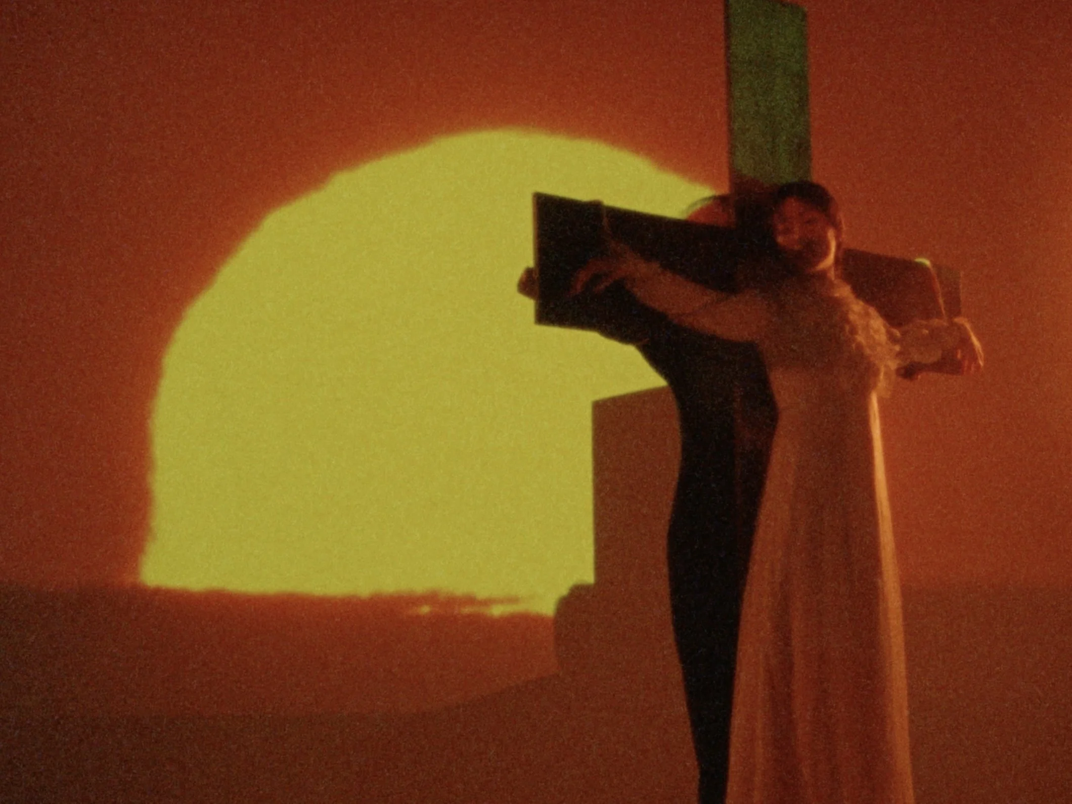 Person dressed as Jesus Christ on cross, with a yellow sun projection in the background.