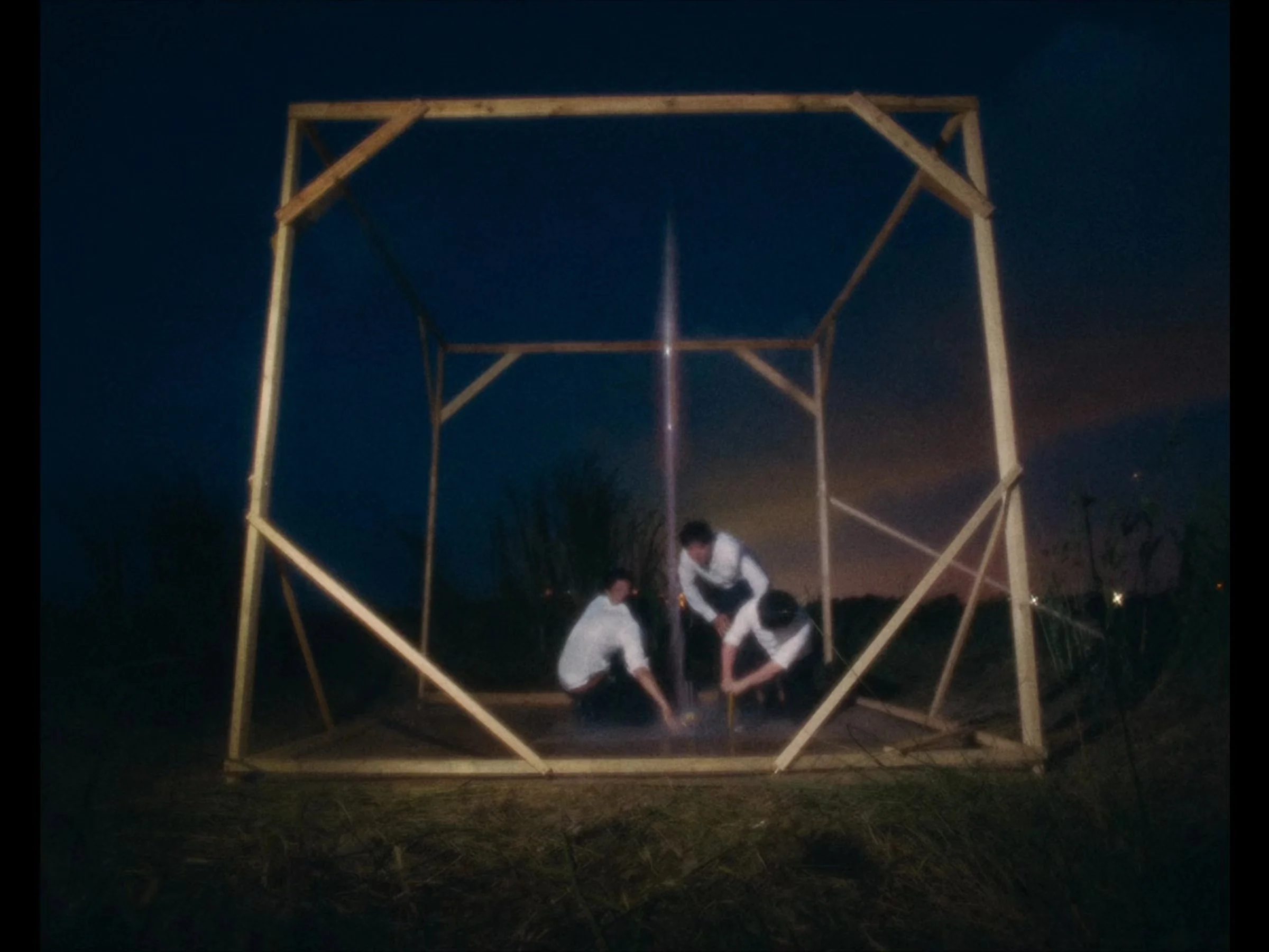 Three construction workers installing a large wooden frame structure outdoors at night, under a dark sky with clouds.