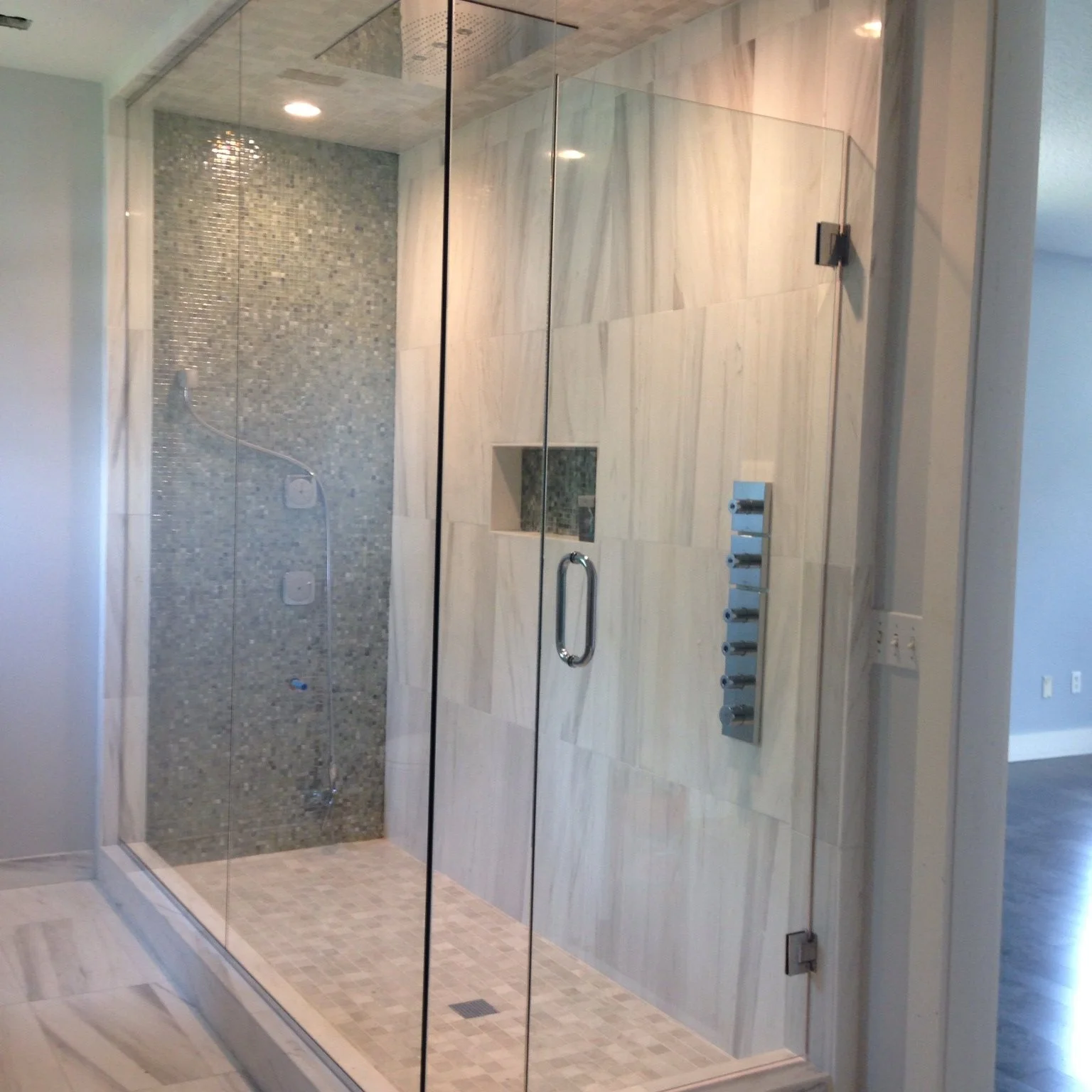 Modern walk-in shower with glass enclosure, tiled walls, mosaic and stone floor, and a built-in niche for toiletries.